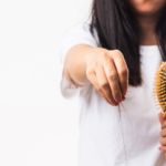 A woman holding a comb and strands of fallen hair in her hand against a white background, highlighting hair loss concerns.
