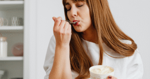 A thoughtful woman sitting at a table, eating comfort food alone, illustrating emotional eating and the connection between emotions and eating habits.